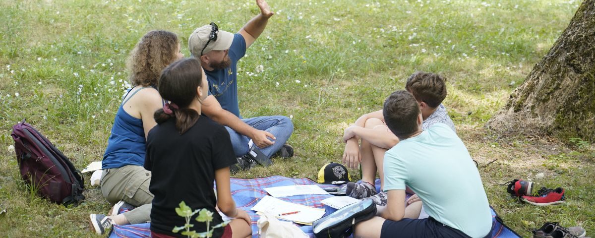 Študenti Letnej školy mladých vedcov 2023 sedia na tráve a rozprávajú sa.