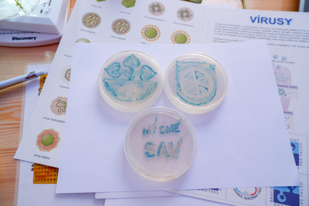 Obrázky v Petriho miskách nakreslené baktériami, logo SAV, logo Trnavy a nápis My sme SAV.